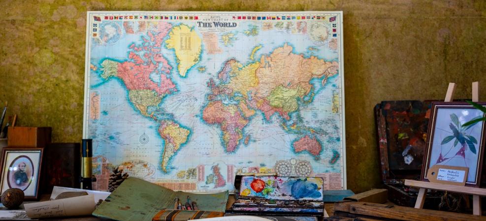 Map of world leaning on wall of study on desk with books, pencils and paint