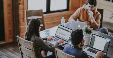 3 people sitting on wooden chairs at table working on laptops