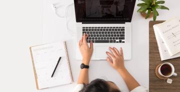 Woman on laptop with diary open and a coffee on desk