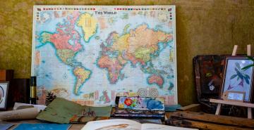 Map of world leaning on wall of study on desk with books, pencils and paint